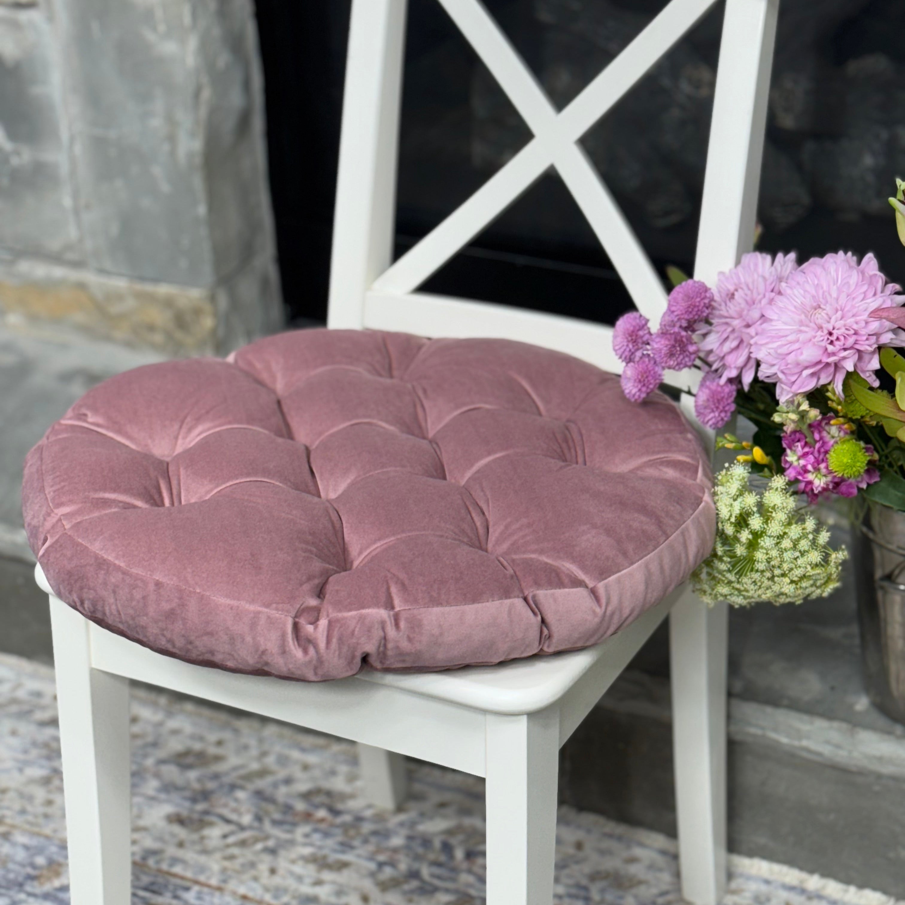 White chair with a purple cushion and a flower arrangement on a stone floor.